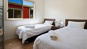 A hotel room with two beds, a window, a nightstand with a lamp, and a view of the outside. - Seaview Beach House 2 (BERMAGUI)