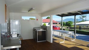 A kitchen with stainless steel appliances, a window, and a balcony with a view of houses and mountains. - Seaview Beach House 2 (BERMAGUI)
