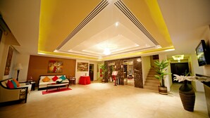 A spacious lobby with a high ceiling, a central light fixture, a sofa with colorful cushions, and a staircase leading to an upper level. - Dunes View Muscat  Hotel Apartments  (Muscat)