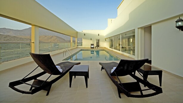 A rooftop pool area with lounge chairs and a small table, overlooking a desert landscape. - Dunes View Muscat  Hotel Apartments  (Muscat)