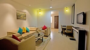 A modern living room with a sofa set, a coffee table, and a dining area with a TV mounted on the wall. - Dunes View Muscat  Hotel Apartments  (Muscat)