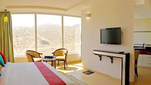 A hotel room with a large bed, a desk, a television, and a view of the desert. - Dunes View Muscat  Hotel Apartments  (Muscat)