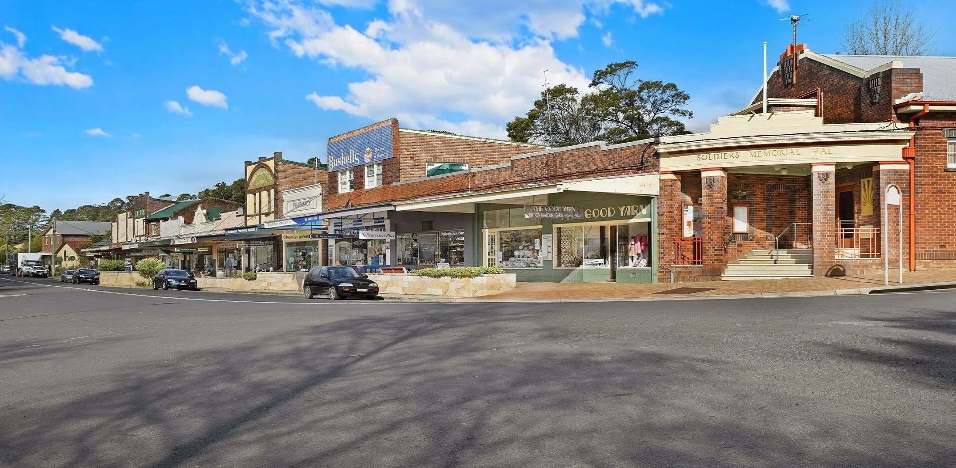 A street view with a Soldiers' Memorial Hall, a pharmacy, and a store named 'The Good Yarn'.