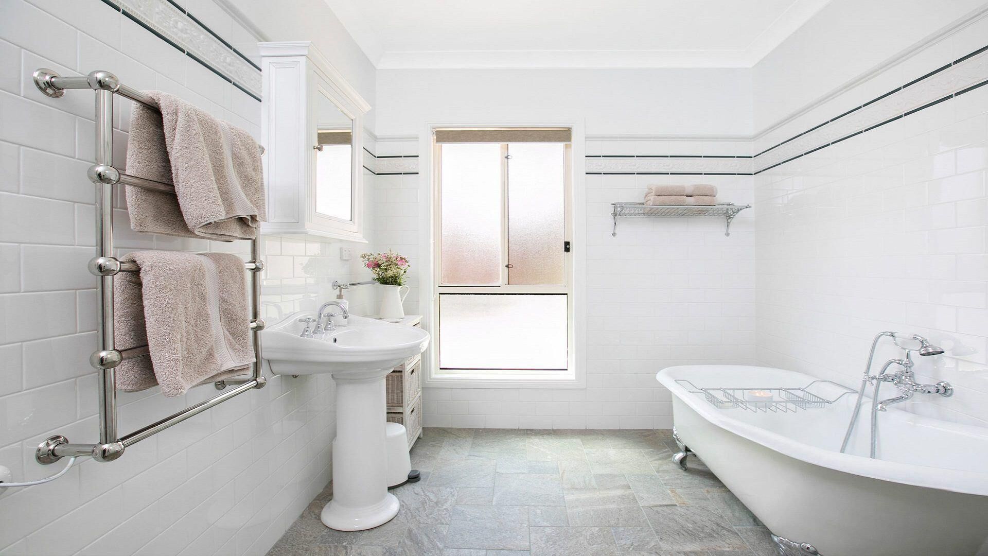 A bathroom with a white sink, a freestanding bathtub, and a towel rack with multiple towels.