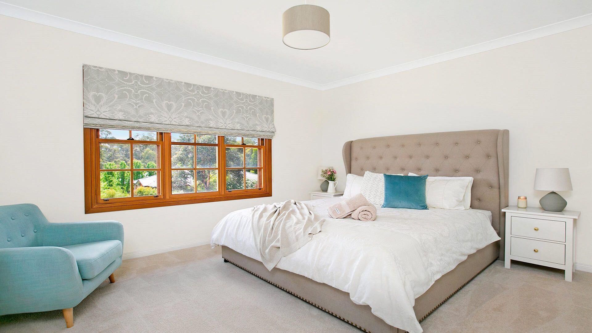 A bedroom with a large bed, a window with a view, a chair, and a bedside table with a lamp.