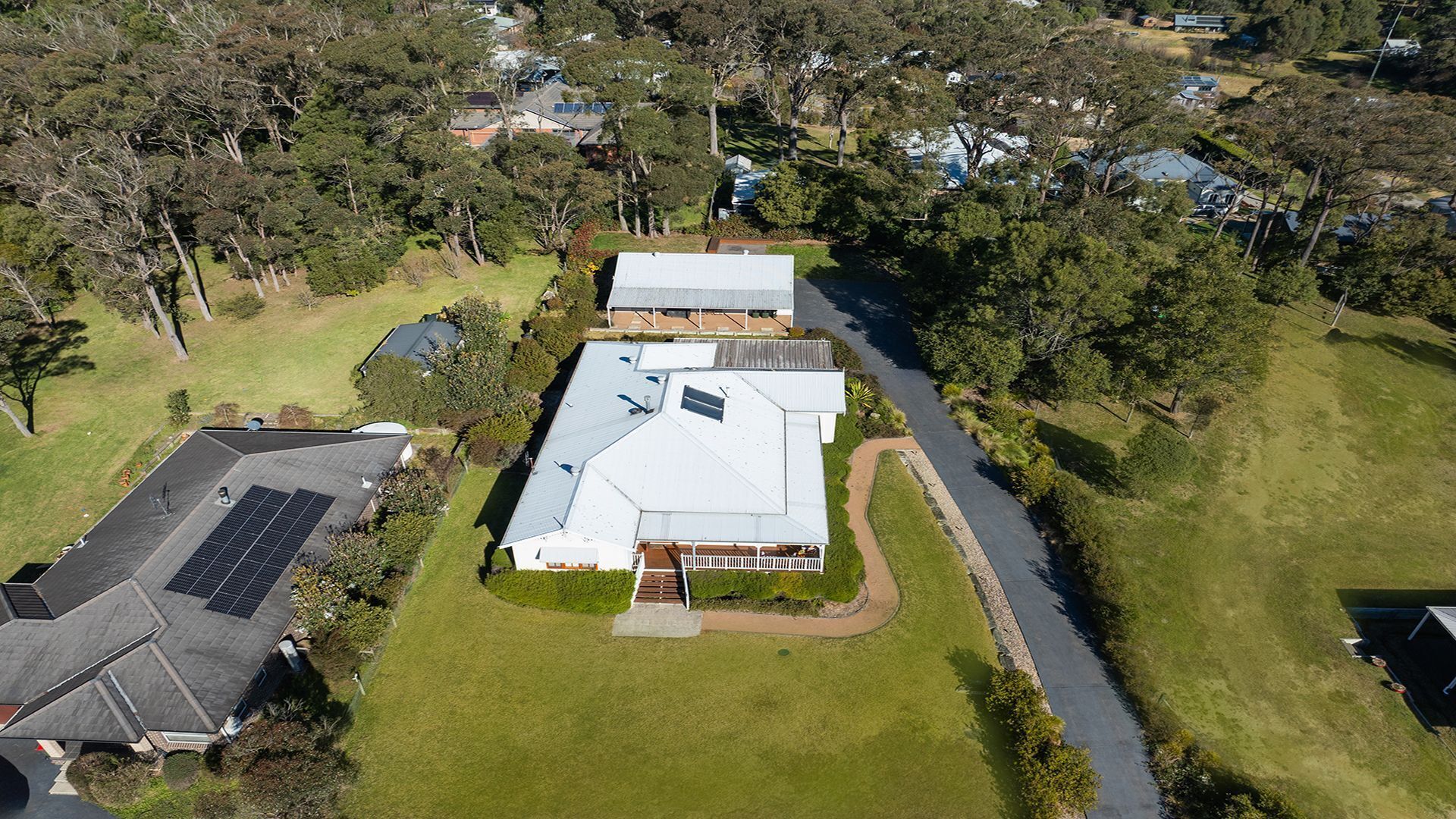An aerial view of a residential property with a large house, solar panels, and a well-maintained lawn.