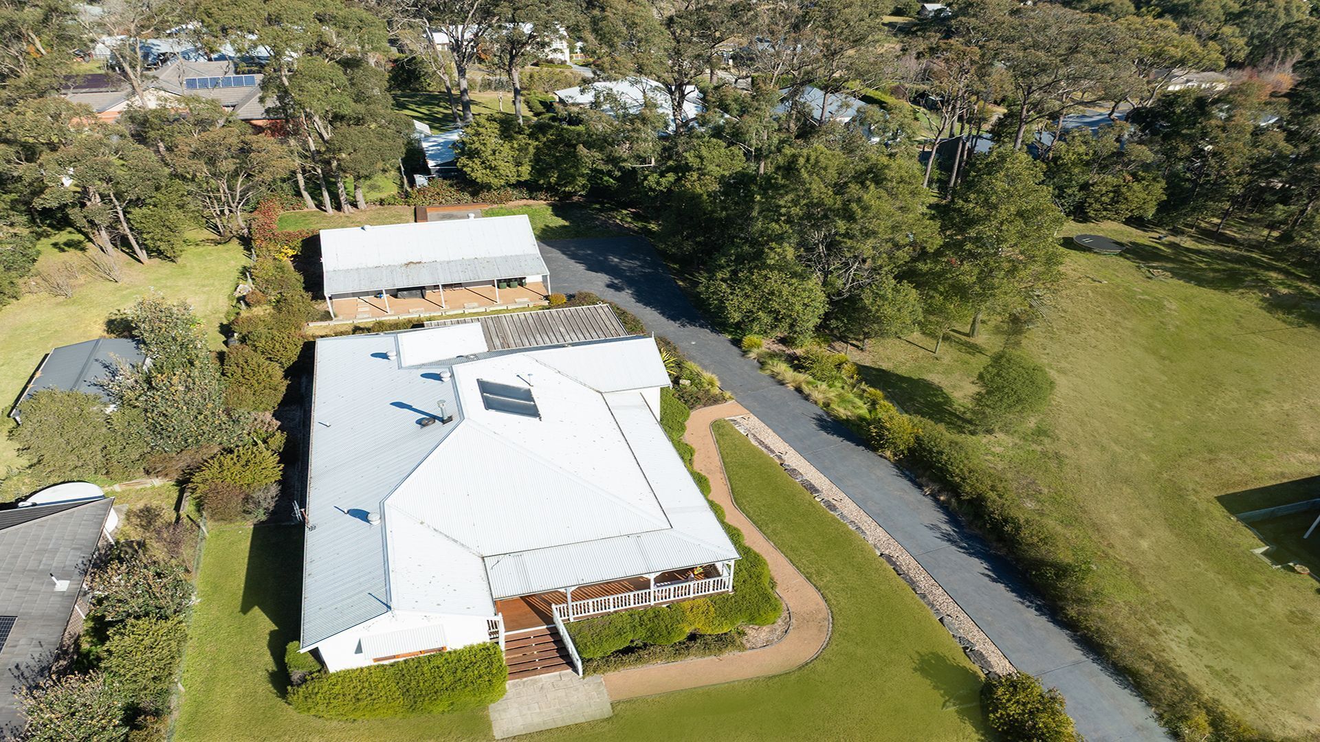 An aerial view of a residential property with a large house, a covered patio, and a well-maintained lawn.
