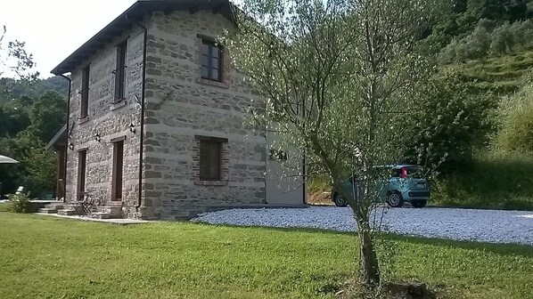 Un edificio de piedra con techo inclinado, camino de grava y un pequeño árbol en primer plano.