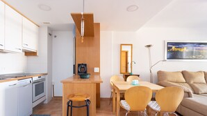 Een compacte keuken met een houten bar, een eethoek met een tafel en stoelen, en een zithoek met een bank.