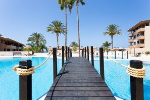 A wooden deck leading to a pool with palm trees and a clear blue sky. - Apartment with pool and WiFi in Playa Paraiso (Tenerife)