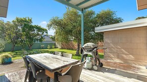 Un patio con mesa y sillas de madera, una parrilla y un área cubierta.