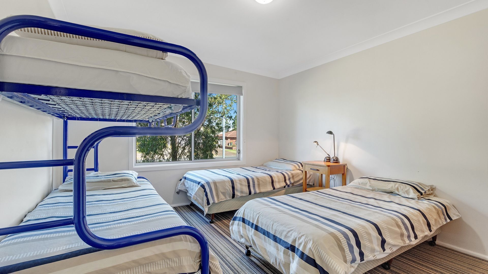 Una camera del dormitorio con letti a castello, due letti singoli, un piccolo tavolo di legno con una lampada e una finestra che offre vista all'esterno.