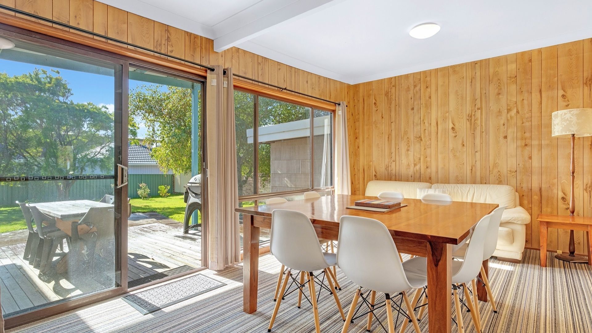 A room with a wooden interior, a sliding glass door leading to an outdoor area, a dining table with chairs, and a sofa.