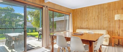 A room with a wooden interior, a sliding glass door leading to an outdoor area, a dining table with chairs, and a sofa.