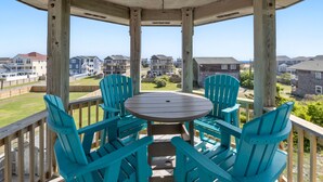 Un espacio al aire libre techado con una mesa redonda y cuatro sillas Adirondack turquesa, con vistas a un barrio residencial.