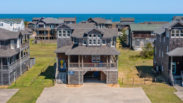 Un área residencial costera con varias casas de dos pisos, una estructura de madera central con balcón, y vista al océano.