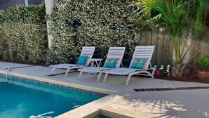 Une piscine avec un jacuzzi, des chaises longues et une haie en arrière-plan.