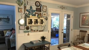 Un coin repas avec une table et des chaises en bois, une petite table d’appoint en osier et un mur décoré d’objets et de tableaux encadrés sur le thème de la marine.