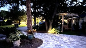 Un espace extérieur pavé, agrémenté de plantes en pot et surmonté d’une pergola.