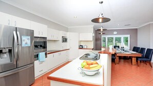 Une cuisine moderne dotée d’appareils électroménagers en acier inoxydable, un îlot central agrémenté de fruits et un coin repas avec une table et des chaises.