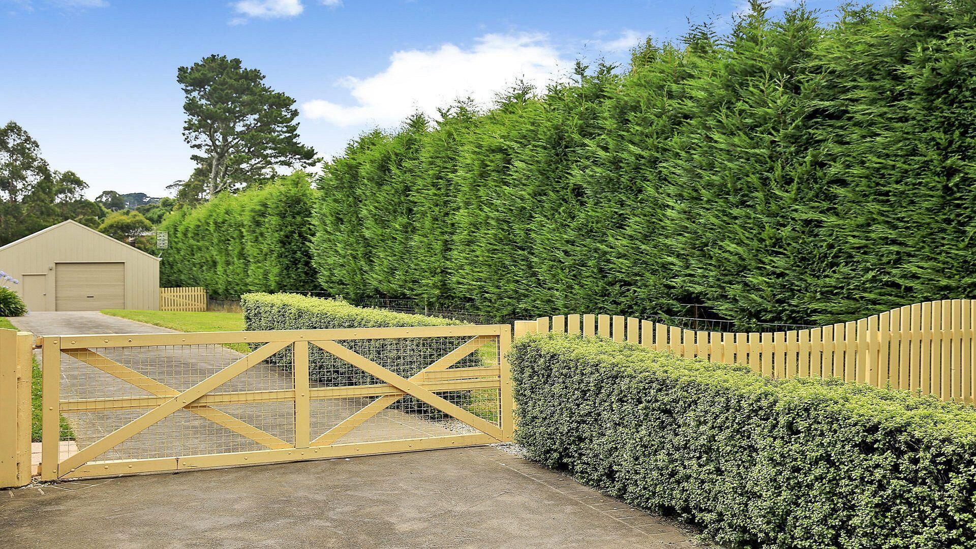 A gated entrance with a wooden fence, a hedge, and a building in the background.
