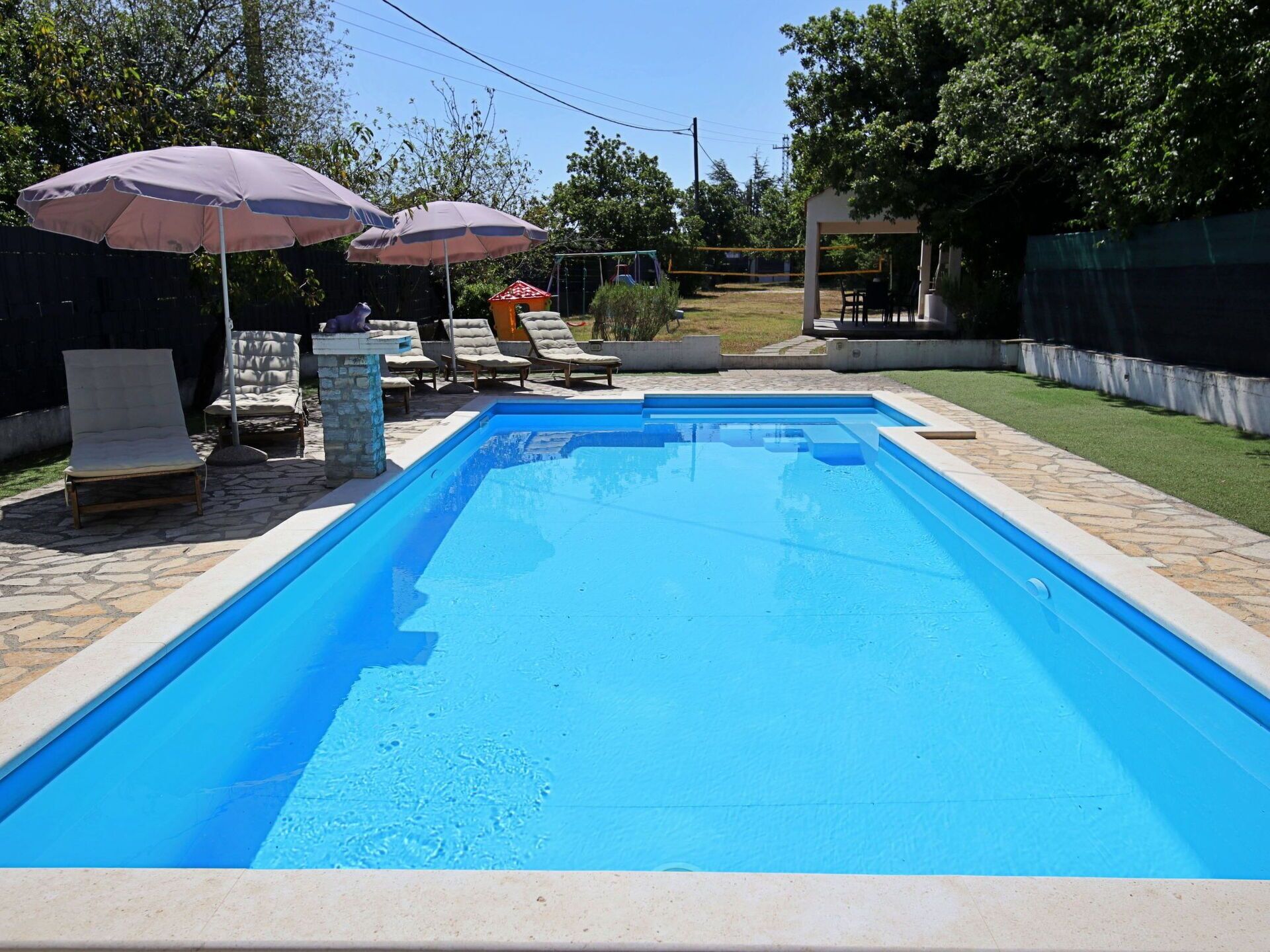 Piscina retangular com borda de pedra, cercada por espreguiçadeiras e guarda-sóis.