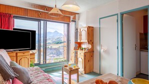 A cozy living room with a large TV, a wooden cabinet, and a view of mountains through the window. - Nice apartment for 4 people with WIFI, TV and balcony (La Toussuire)