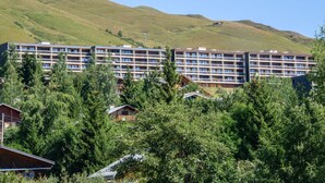 A multi-story hotel with balconies, surrounded by lush greenery and hills. - Nice apartment for 4 people with WIFI, TV and balcony (La Toussuire)