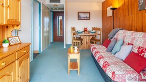 A cozy room with a wooden wardrobe, a dining table with chairs, a sofa with patterned cushions, and a hanging light fixture. - Nice apartment for 4 people with WIFI, TV and balcony (La Toussuire)
