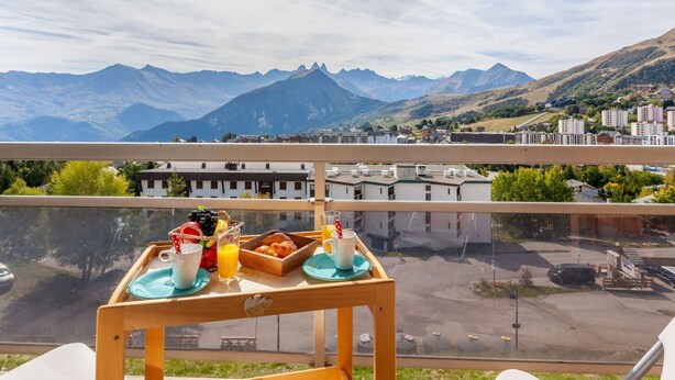 A balcony with a table set for breakfast, overlooking a mountainous landscape and a town. - Nice apartment for 4 people with WIFI, TV and balcony (La Toussuire)