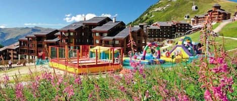 A mountain resort with wooden buildings, a colorful play area, and a ski lift in the background.