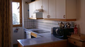 A kitchen with white cabinets, a microwave, a toaster, and a window with curtains. - Pierre De Soleil -  Ski in/out, next to ski school, shops/restaurants -free wifi (Mâcot-la-Plagne)