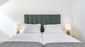 A double bed with a green upholstered headboard, white bedding, and two bedside lamps.