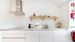 A modern kitchen with white cabinets, a stainless steel range hood, wooden shelves with kitchenware, and a fire extinguisher mounted on the wall.