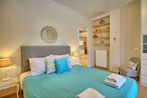 A bedroom with a bed, pillows, a bedside lamp, a mirror, and a view into the kitchen.