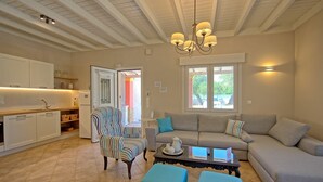 A living room with a sofa, armchairs, and a coffee table. There is a kitchen area with cabinets and a refrigerator. - Beach Villa Joanna - Luxury Villa rental in Corfu, Greece (Acharavi)