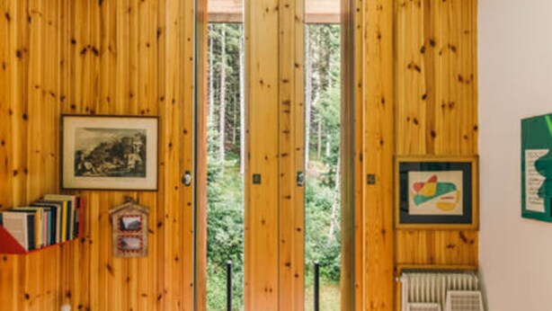 Una habitación con paredes de madera y un ventanal grande. Hay estanterías con libros y cuadros en la pared.