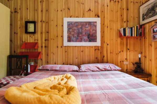 A wooden-paneled room with a bed, a red chair, a bookshelf, and a painting on the wall.