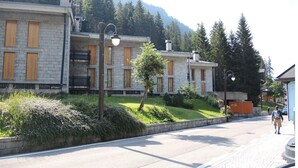 Una hilera de edificios de piedra con contraventanas de madera, un camino pavimentado y una persona caminando.