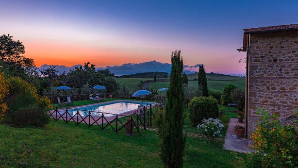 Area piscina con ombrelloni, un edificio in pietra e vista sulla campagna al crepuscolo.
