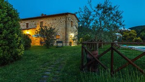 Un edificio in pietra con un ingresso ben illuminato, un cortile lastricato di erba e una zona piscina.