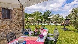 Area pranzo all'aperto con parete in pietra, piscina sullo sfondo e barbecue.