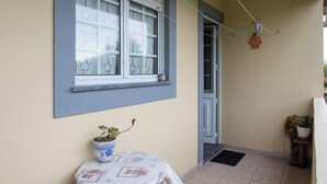 Un piccolo balcone con una pianta in vaso, una finestra con persiane decorative e una porta.
