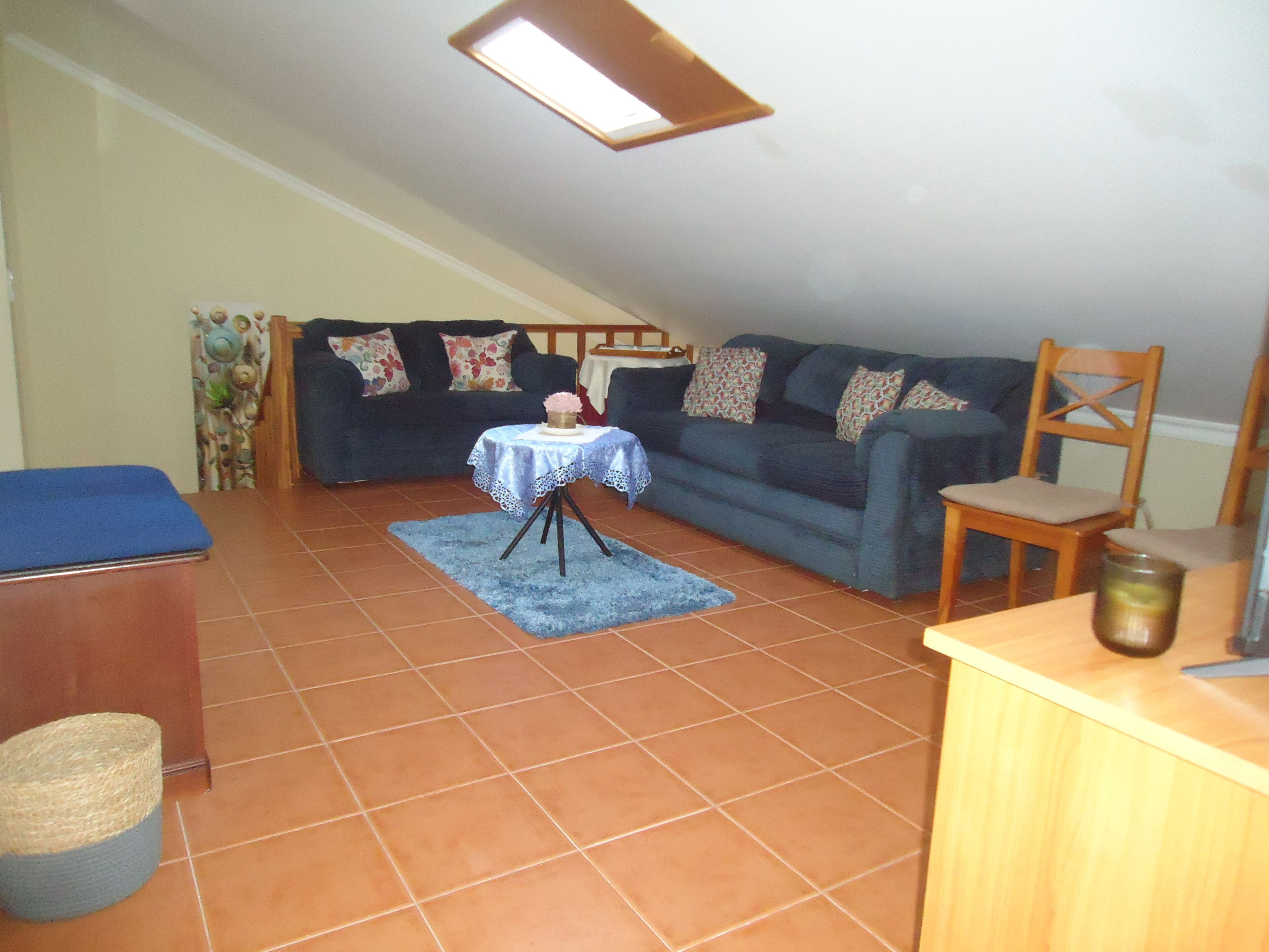 A living room with a blue sofa, a small table with a vase, a wooden chair, and a blue rug.