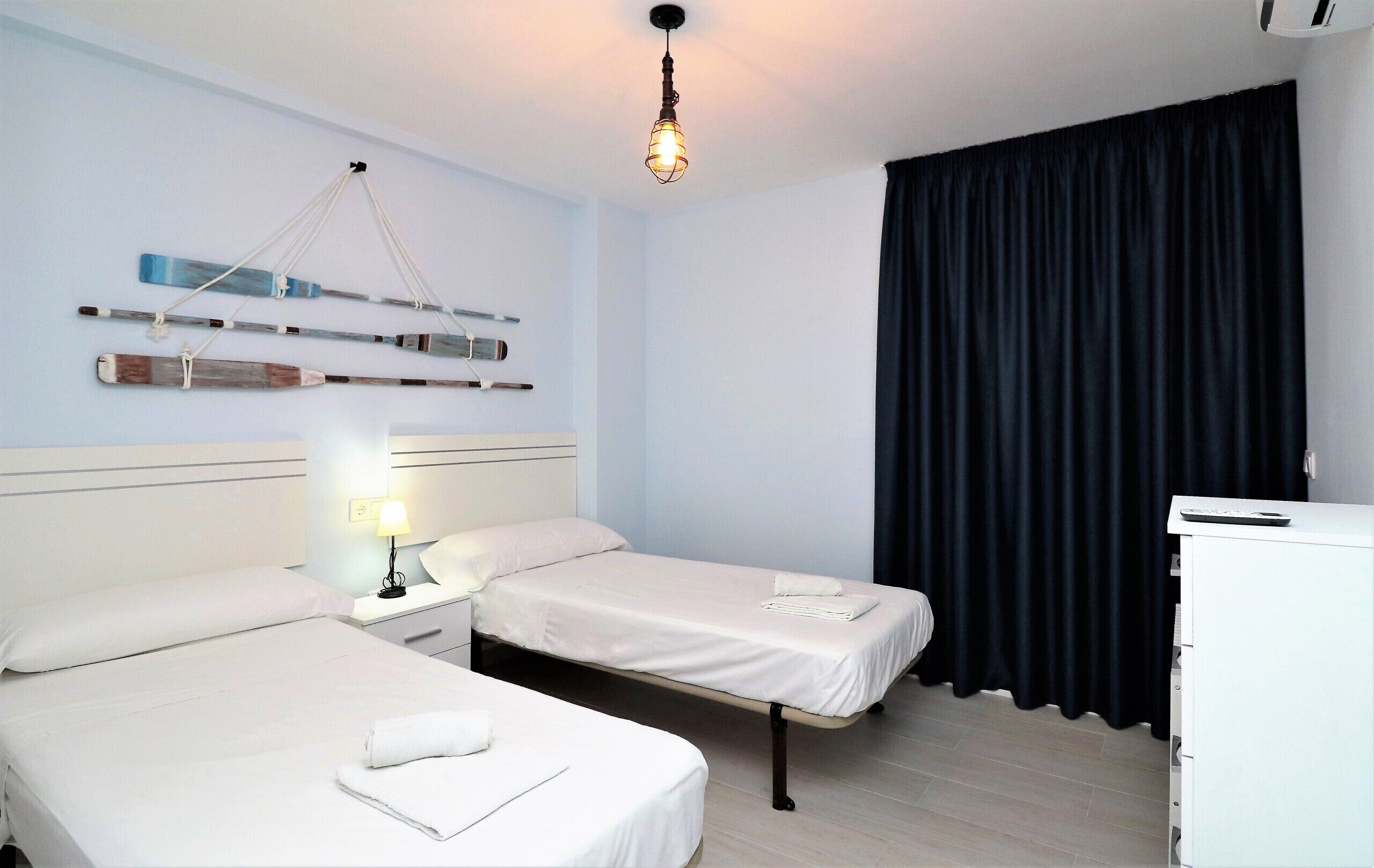 Een hotelkamer met twee bedden, een nachtkastje met lamp, een bureau en een zwart gordijn.