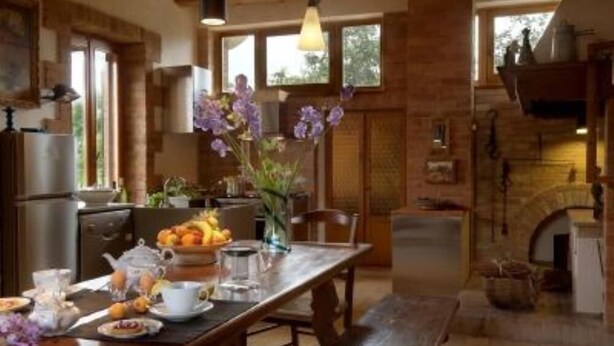 A rustic kitchen with a wooden table set for breakfast, a hanging light fixture, and a brick fireplace.