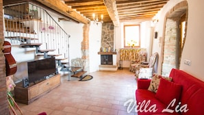 A cozy living room with a fireplace, wooden beams, a red sofa, and a television on a wooden cabinet. - Private House with Exclusive Swimming Pool Heated and Amazing View (Boccheggiano)