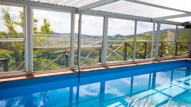 An indoor swimming pool with a view of a vineyard and hills. - Private House with Exclusive Swimming Pool Heated and Amazing View (Boccheggiano)