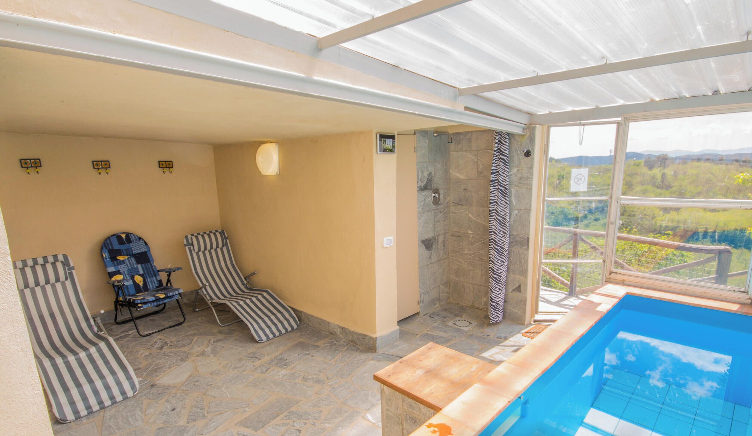 A sunlit indoor swimming pool area with lounge chairs and a stone-tiled floor.