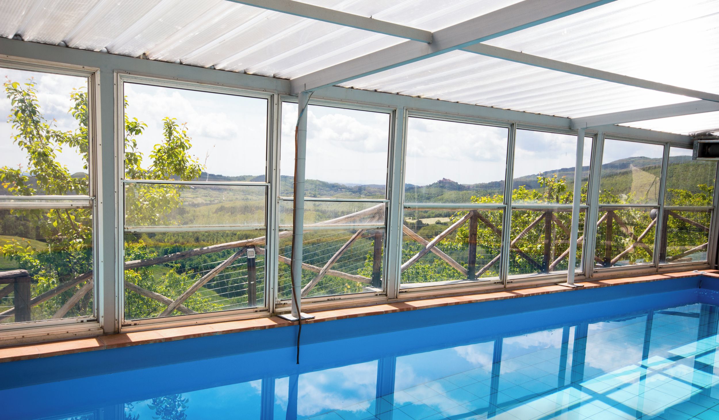 An indoor swimming pool with a view of a vineyard and hills.
